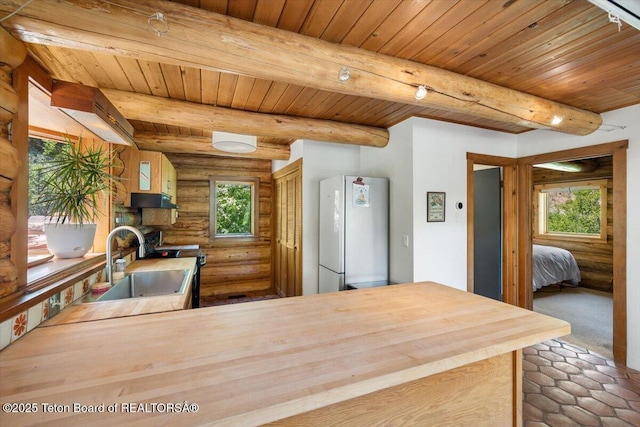 6250 W Paintbrush Trl, Wilson, WY 83014 - kitchen with freestanding refrigerator, log walls, healthy amount of natural light, a wooden ceiling with exposed beams, and under cabinet range hood