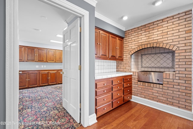 4976 S 49th, Idaho Falls, ID 83406 - kitchen with ornamental molding, brown cabinetry, tile counters, wood finished floors, and brick wall
