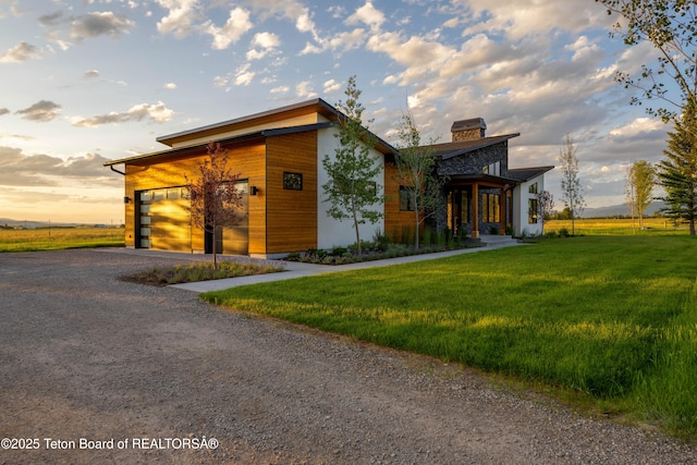 9346 Basin Dr, Victor, ID 83455 - contemporary home with gravel driveway, a front yard, an attached garage, and a chimney