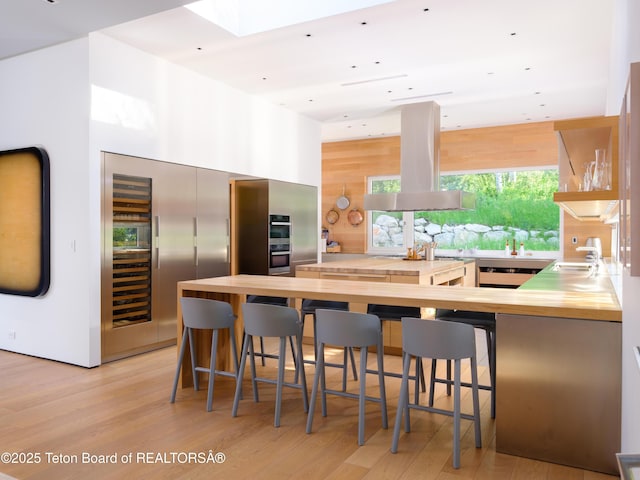 7970 N Granite Ridge Rd, Teton Village, WY 83025 - kitchen featuring island exhaust hood, wooden counters, light wood-type flooring, a kitchen breakfast bar, and a skylight