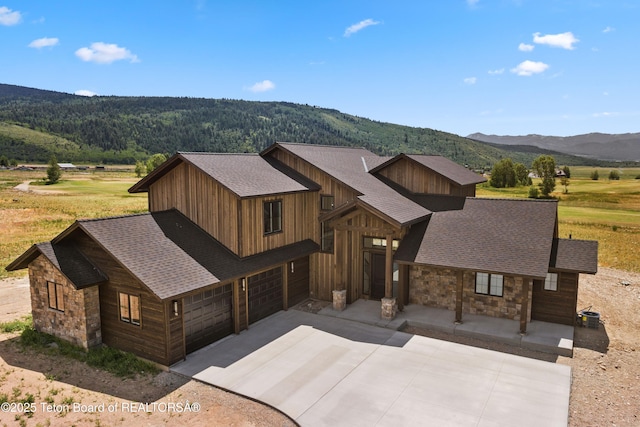 555 Silver Fox Ln, Victor, ID 83455 - view of front of home with stone siding, concrete driveway, a shingled roof, a mountain view, and an attached garage
