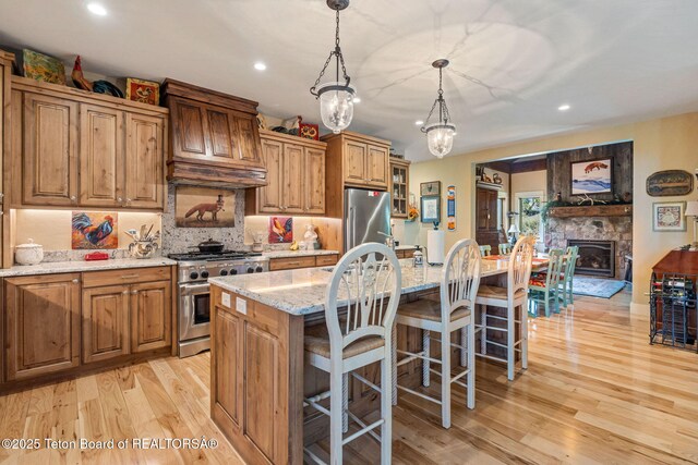 6289 Fox Meadows Dr, Victor, ID 83455 - kitchen with stainless steel appliances, light wood finished floors, light stone counters, a kitchen island with sink, and a breakfast bar area