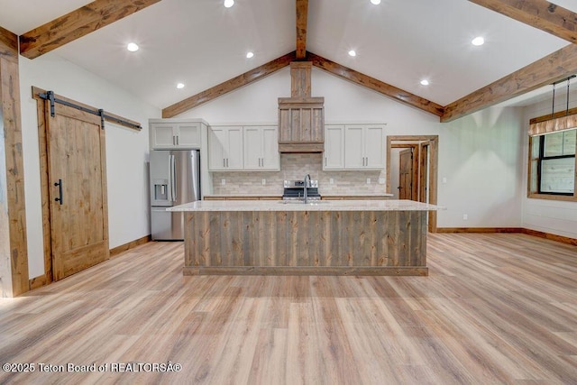 245 Pond Dr, Victor, ID 83455 - kitchen with stainless steel fridge with ice dispenser, light wood finished floors, a barn door, a large island with sink, and tasteful backsplash