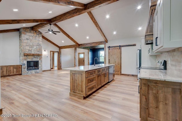 245 Pond Dr, Victor, ID 83455 - kitchen featuring a stone fireplace, a barn door, a ceiling fan, an island with sink, and light stone counters