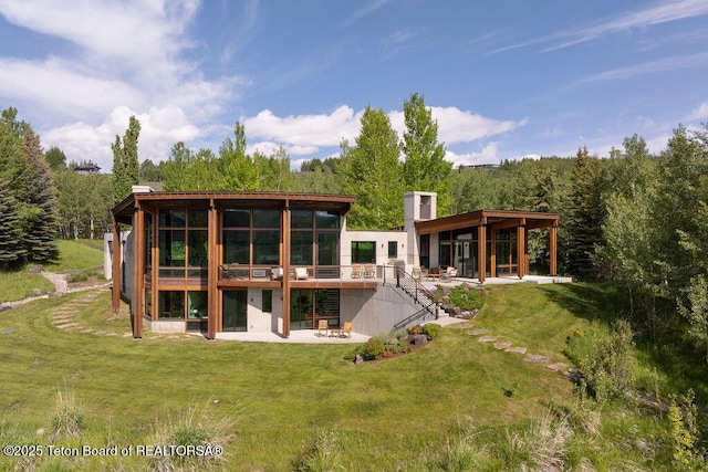 1955 W Bohnetts Rd, Jackson, WY 83001 - rear view of house featuring a patio area, a lawn, a wooded view, a wooden deck, and a chimney