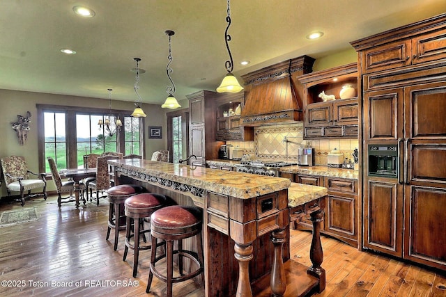 70 Hastings Dr, Victor, ID 83455 - kitchen featuring paneled fridge, an island with sink, premium range hood, hardwood / wood-style flooring, and backsplash