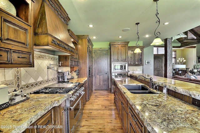 70 Hastings Dr, Victor, ID 83455 - kitchen featuring appliances with stainless steel finishes, light wood-style flooring, premium range hood, recessed lighting, and light stone countertops