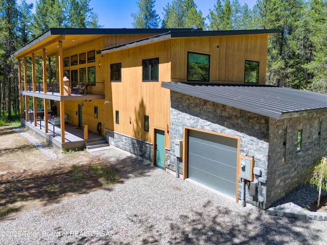 4327 Bridger Rdg, Ashton, ID 83420 - view of property exterior featuring an attached garage, stone siding, gravel driveway, a balcony, and a metal roof