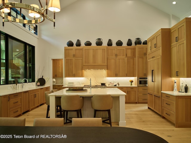 3220 N Teton Pines Dr, Wilson, WY 83014 - kitchen featuring high vaulted ceiling, light countertops, a kitchen bar, a kitchen island with sink, and light wood finished floors