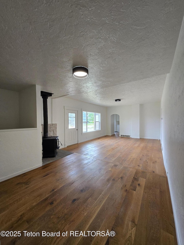 6270 S 3rd St, Tetonia, ID 83452 - unfurnished living room with wood-type flooring, a textured ceiling, a wood stove, a textured wall, and arched walkways
