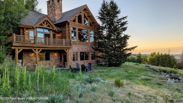 8157 Ripplinger Rd, Driggs, ID 83422 - back of house at dusk featuring log exterior, stone siding, a chimney, and a deck