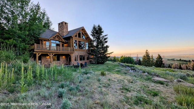 8157 Ripplinger Rd, Driggs, ID 83422 - back of house at dusk featuring log siding, stone siding, a deck, and a chimney
