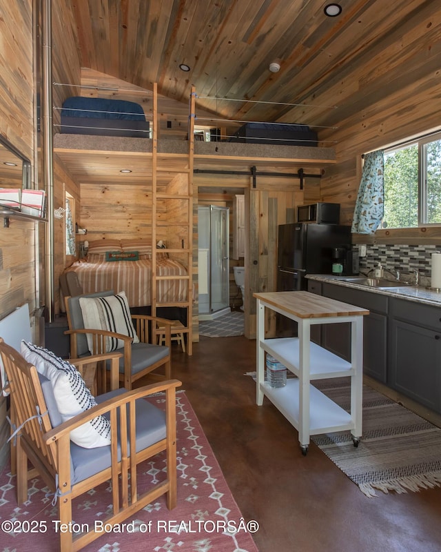 66 Elkhorn Dr, Thayne, WY 83127 - kitchen featuring wooden walls, a barn door, finished concrete flooring, freestanding refrigerator, and lofted ceiling