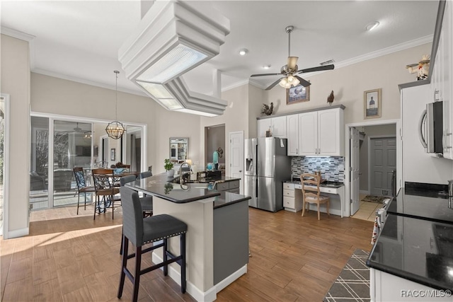 kitchen featuring a center island with sink, a kitchen breakfast bar, ceiling fan, stainless steel appliances, and white cabinets