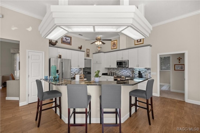 kitchen with white cabinetry, ornamental molding, stainless steel appliances, and a kitchen breakfast bar