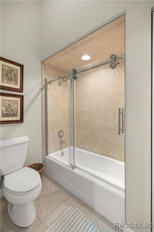 bathroom featuring tile patterned flooring, toilet, and combined bath / shower with glass door