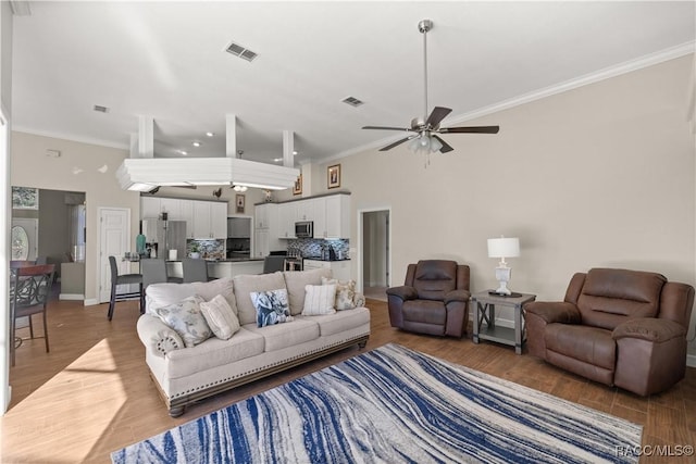 living room featuring crown molding, ceiling fan, hardwood / wood-style floors, and a towering ceiling