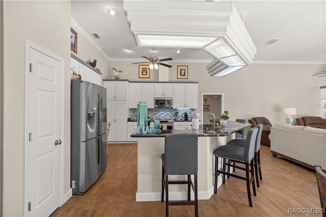 kitchen featuring crown molding, a breakfast bar, white cabinetry, backsplash, and stainless steel appliances