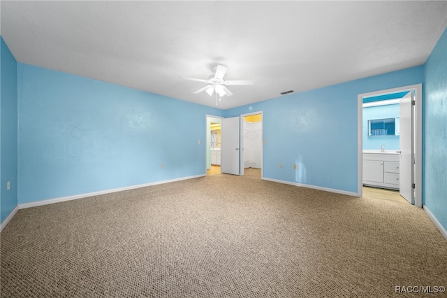 unfurnished bedroom with ceiling fan, connected bathroom, a closet, light colored carpet, and a walk in closet