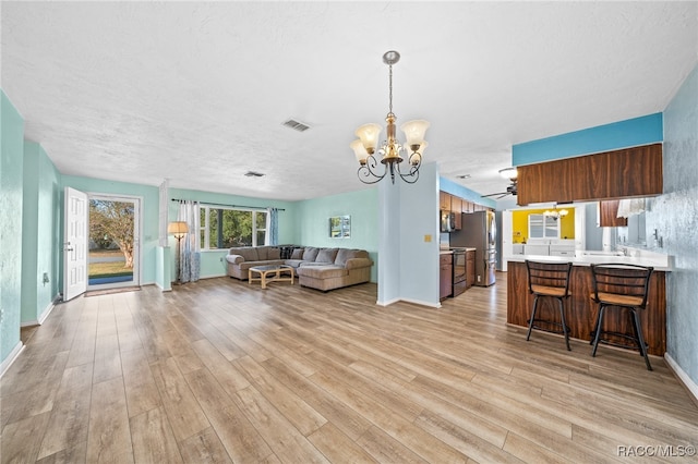 living room featuring ceiling fan with notable chandelier, a textured ceiling, and light wood-type flooring