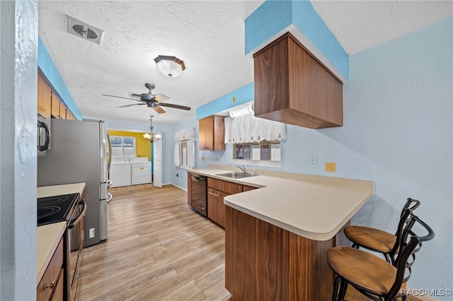 kitchen featuring light hardwood / wood-style floors, kitchen peninsula, separate washer and dryer, black appliances, and sink