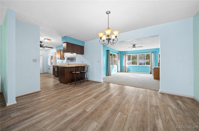 unfurnished living room with ceiling fan with notable chandelier, sink, and light wood-type flooring