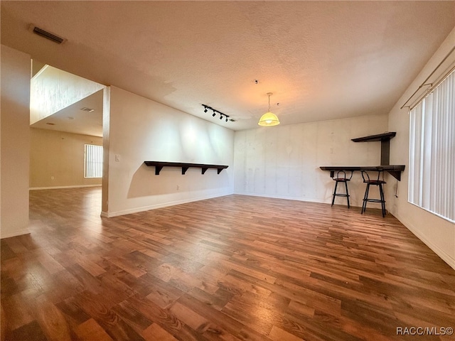 interior space with a textured ceiling, dark hardwood / wood-style flooring, and rail lighting