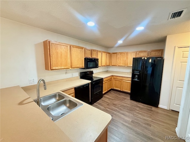 kitchen featuring light brown cabinets, black appliances, wood-type flooring, sink, and kitchen peninsula