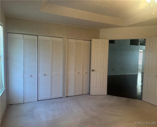 unfurnished bedroom featuring multiple closets, a raised ceiling, and carpet