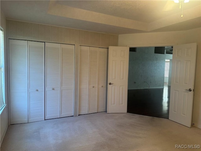 unfurnished bedroom featuring a tray ceiling, multiple closets, and light colored carpet