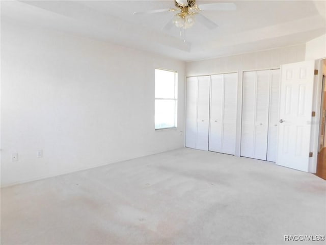 unfurnished bedroom with ceiling fan, a tray ceiling, carpet, and two closets