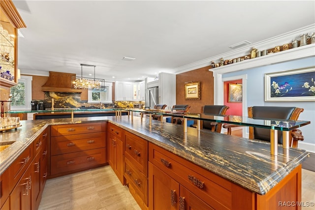 kitchen featuring stainless steel refrigerator, hanging light fixtures, tasteful backsplash, a kitchen breakfast bar, and ornamental molding