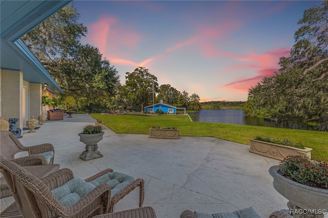 patio terrace at dusk with a water view and a lawn