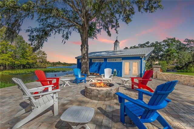 patio terrace at dusk featuring french doors, a water view, and an outdoor fire pit