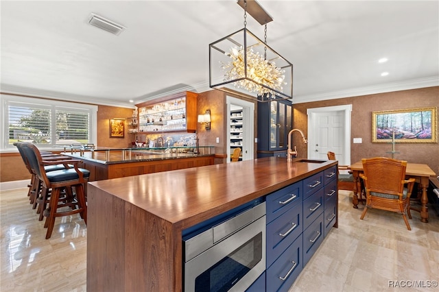 kitchen with blue cabinetry, stainless steel microwave, sink, a center island with sink, and ornamental molding