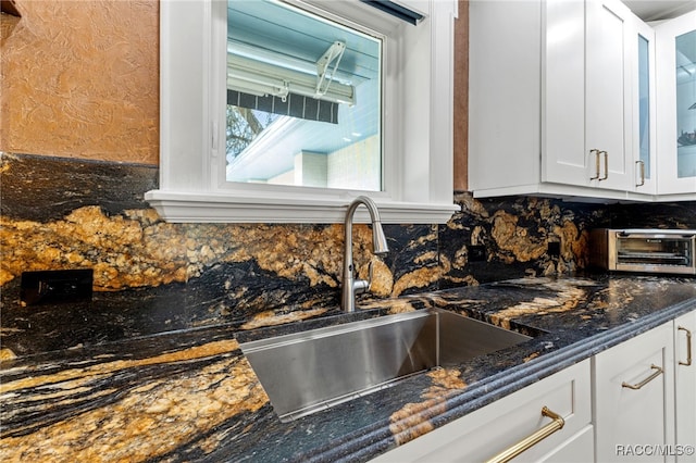 kitchen with white cabinets, tasteful backsplash, dark stone counters, and sink