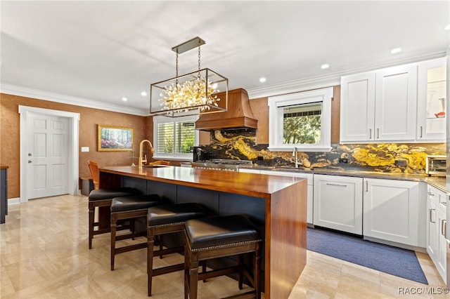 kitchen with white cabinets, a breakfast bar, premium range hood, and an island with sink