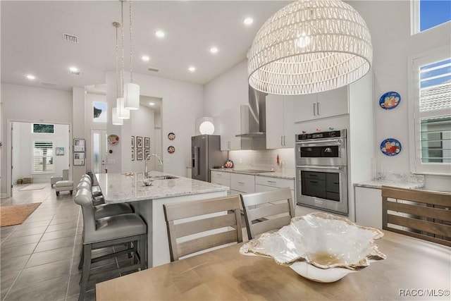 kitchen featuring sink, hanging light fixtures, a center island with sink, stainless steel appliances, and white cabinets