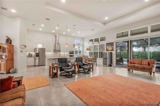 living room featuring light tile patterned flooring, a towering ceiling, a raised ceiling, and sink