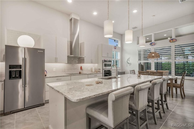 kitchen with a kitchen island with sink, wall chimney exhaust hood, white cabinets, and appliances with stainless steel finishes