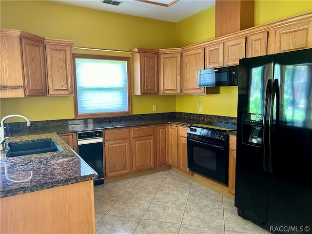 kitchen with dark stone countertops, sink, light tile patterned flooring, and black appliances