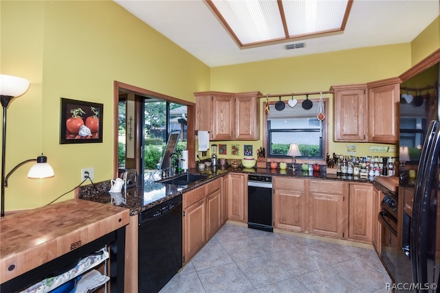 kitchen featuring dark stone counters, black appliances, sink, hanging light fixtures, and light tile patterned flooring