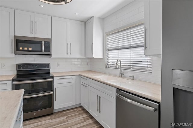 kitchen with white cabinets, appliances with stainless steel finishes, light wood-type flooring, and sink