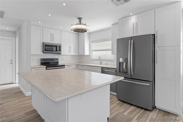 kitchen featuring white cabinets, a center island, stainless steel appliances, and light hardwood / wood-style flooring