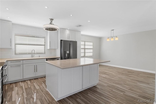 kitchen with a healthy amount of sunlight, a kitchen island, stainless steel fridge with ice dispenser, and hanging light fixtures