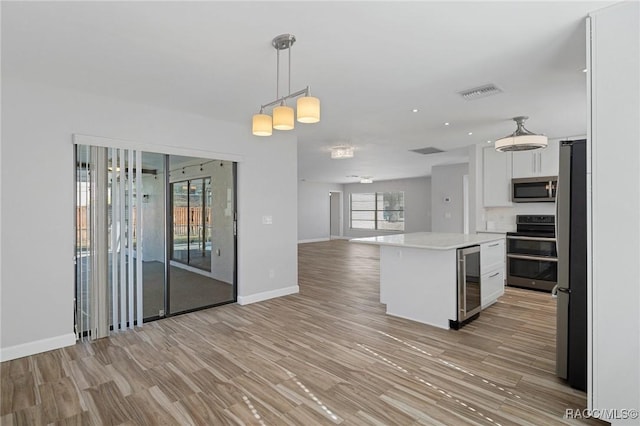 kitchen with white cabinets, hanging light fixtures, light wood-type flooring, appliances with stainless steel finishes, and a kitchen island