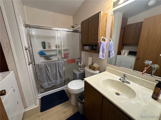 bathroom featuring toilet, a stall shower, wood finished floors, washer / dryer, and vanity