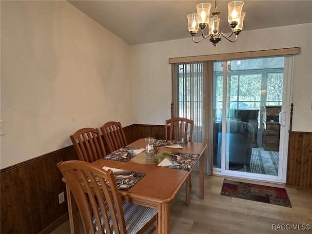 dining area featuring a notable chandelier, wood finished floors, wainscoting, and wood walls