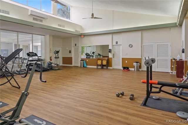 workout area featuring ceiling fan, light hardwood / wood-style floors, and a towering ceiling