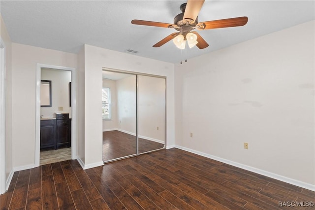 unfurnished bedroom featuring ensuite bath, dark wood-type flooring, a closet, and ceiling fan